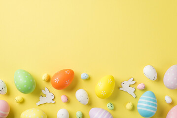 Top view of multicolored Easter eggs and quail ones with two white rabbits situated on the isolated yellow background copyspace