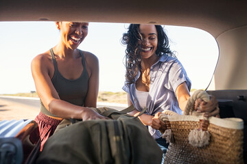 Happy smiling woman friends put bag and luggage into car trunk