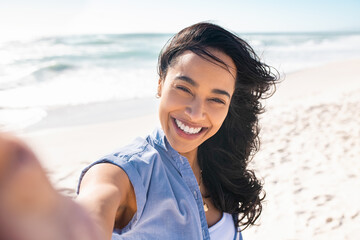 Laughing latin woman on beach taking selfie during summer vacation