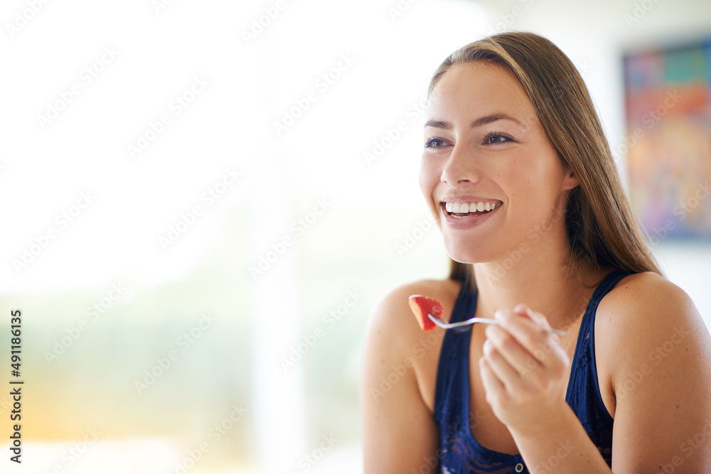 Wall mural Nature has the best takeaways. Shot of a young woman eating a bowl of strawberries at home.