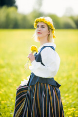 Young woman in national clothes wearing yellow dandelion wreath in spring field. Springtime