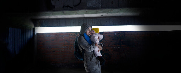 Exhausted mother holding her child in arms in the bomb shelter - obrazy, fototapety, plakaty