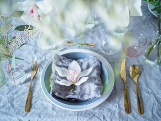 Relaxed and fresh table setting with flowers. Grey linen tablecloth and a napkin, golden cutlery...