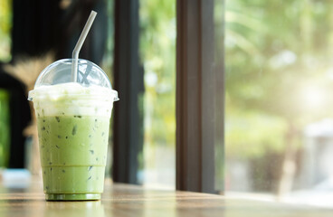 Iced green tea with frothed milk in a plastic cup on a wooden table in a coffee shop.