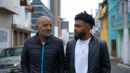 An African father and adult son walking together outside in urban street two people bonding