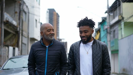 An African father and adult son walking together outside in urban street two people bonding