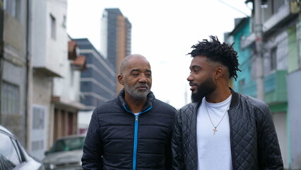 An African father and adult son walking together outside in urban street two people bonding