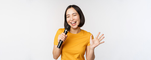 Happy asian girl dancing and singing karaoke, holding microphone in hand, having fun, standing over...