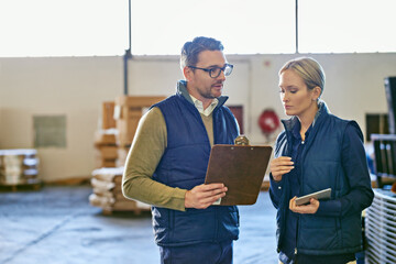 These shipments are a priority. Shot of two people looking at paperwork while working in a...