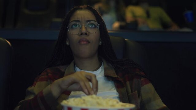 Diverse raced woman sitting in armchair watching a movie at the cinema, eating popcorn