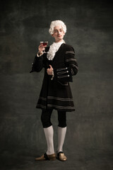 Young man wearing wig and vintage medieval outfit like famous composer isolated on dark green...