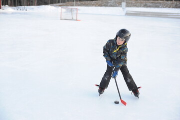 Fototapeta na wymiar A young boy playing and training ice hockey on outdoor ice rink in winter