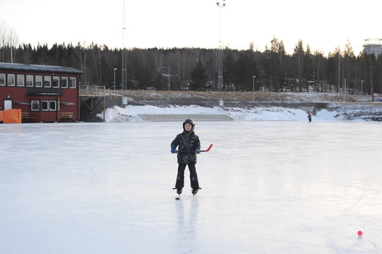 A young boy playing and training ice hockey on outdoor ice rink in winter