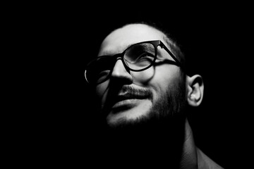 Black and white, close-up dark portrait of young smiling man wearing glasses.