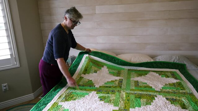 A senior woman shows a quilt that she made and explains the detail, design and process proudly