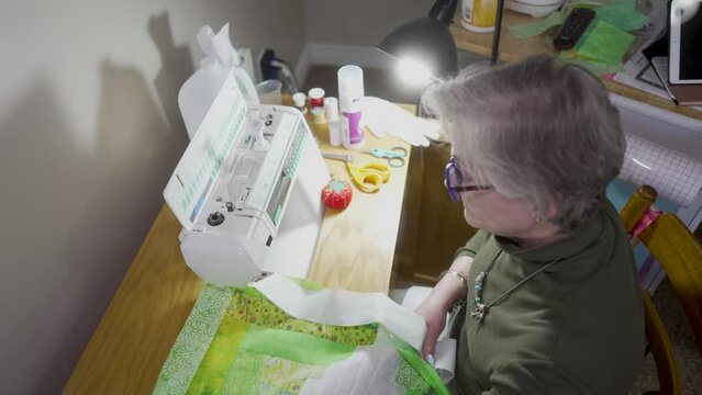 Senior, retired woman sewing quilt blocks together with binding on a sewing machine