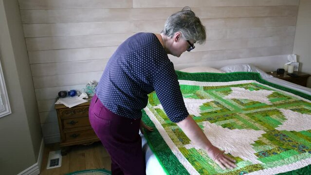 A home craftsman who is a senior woman shows the detail in a quilt she made