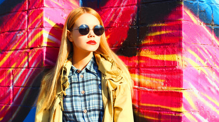 Fashion portrait of beautiful stylish blonde young woman on city street over colorful graffiti background