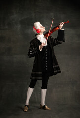 Portrait of young man wearing wig and vintage medieval outfit like famous composer playing violin...