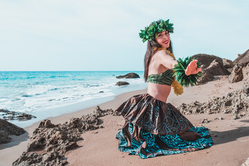 Hula dancer dancing Hawaiian dance. Ballerina in hawaiian, polynesian and tahiti attire dancing on the beach. Woman on her knees dancing on the beach smiling raises her hand. Copy space person. - obrazy, fototapety, plakaty