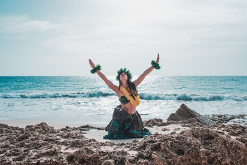 Woman raising arms dancing hula dance on the beach with attire from polynesia and tahiti. Hawaiian woman smiles relaxed on a paradise beach. Exotic beauty with flower crown on her head. - obrazy, fototapety, plakaty
