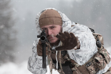 Soldier in winter camouflaged uniform in Modern warfare army on a snow day on forest battlefield...