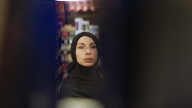 Woman in hijab takes product from the shelf, footage from inside