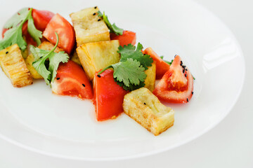 Tomatoes and fried zucchini on a white plate. Healthy vegetable food garnished with herbs. Close-up