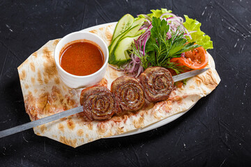 on a kitchen wooden cutting board, shish kebab beef roll on skewers, a bowl with ketchup sauce, on...
