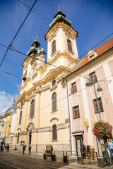 Fototapeta na wymiar Linz, Austria, 27 August 2021: Baroque Ursuline Church of St. Michael with two towers, Narrow picturesque street with colorful buildings in historic center in medieval city at sunny summer day