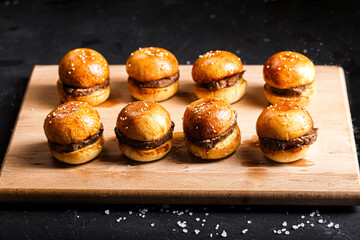 on a kitchen wooden cutting board, a lot of small burgers with a meat patty, a bun with sesame...