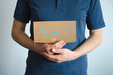 Ein Mann hält ein Schild mit der Botschaft Peace in seinen Händen. Teilabschnitt, Text.