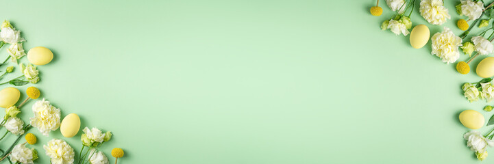 Easter banner. Tender fresh white and yellow flowers and coloured chicken eggs on light green background. Festive spring composition. Blooming holiday mockup. Copy space, top view, flat lay.