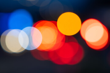 Blurred lights on an busy german inner city street at night time. Colorful unfocused transparent light circles of glowing traffic lights, flickering flash lights in red, yellow, blue and orange. 