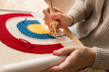 New trend in embroidery Punch needle. Close up of woman creating a handmade decoration for home. Female pushing the punchneedle straight down into the fabric. Hobby, DIY, handycraft concept