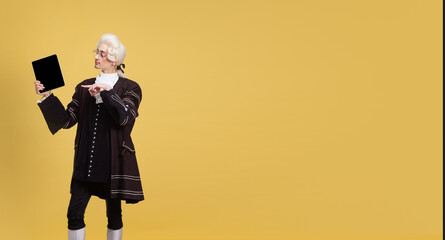 Portrait of young elegant man in white wig and vintage medieval outfit posing isolated on yellow background. Art, beauty, fashion
