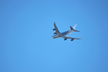 Airplane flying in the clear blue sky, bottom view. Commercial four-engine plane taking off