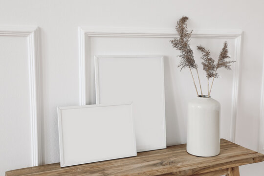 Set of blank white picture frame mockups. Vase with dry reed, grass on old wooden bench. Wall moulding background, trim decor. Elegant home interior decor still life photo. Art dispaly. Side view.