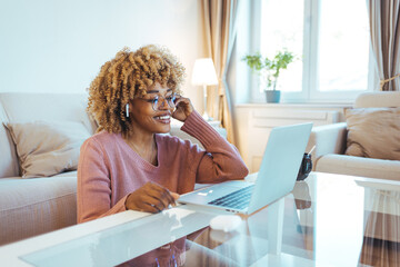 Using her laptop and bluetooth earbuds, the mid adult woman video conferences from home during the...