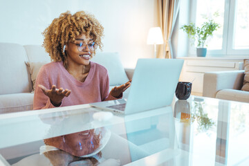 Young woman video calling using a laptop sitting on a sofa wearing earphones. Using laptop and bluetooth earbuds, woman video conferences from home