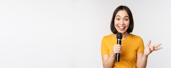Image of young asian woman talking in microphone, perfom with mic, giving speech, standing in...