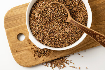 dry buckwheat groats in a white bowl on a wooden board with a wooden spoon, on a white background, top view, close-up