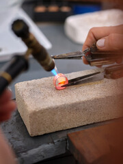 a woman working in her artisan jewelry workshop using a torch on a ring to perform her work on a block of stone