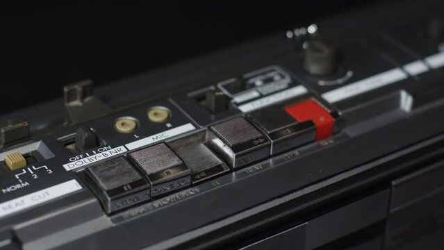 A finger presses the rewind button on a dusty panel on an old tape recorder