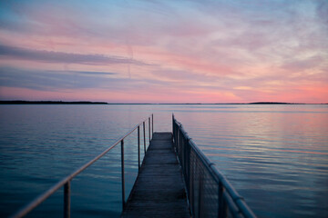 pink sunset at wooden pier on blue sea. view of long jetty stretching to the ocean. water reflection