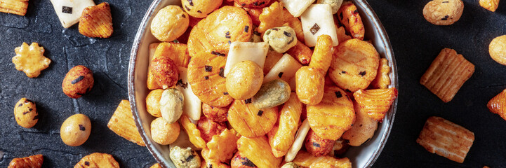Japanese rice crackers in a bowl on a black slate background, panorama, overhead flat lay shot
