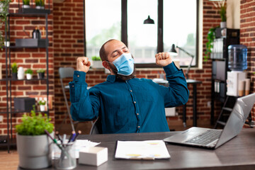 Ambitious entrepreneur with medical protection face mask to prevent infection with coronavirus making happy dance moves after reading business good news. Manager accomplished successful contract