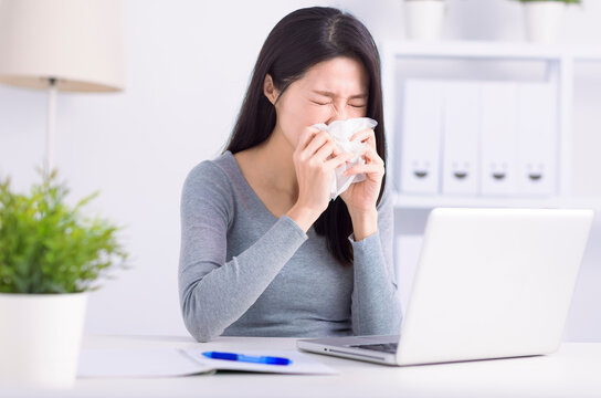 Stressed young  woman sneezing  and working at home office
