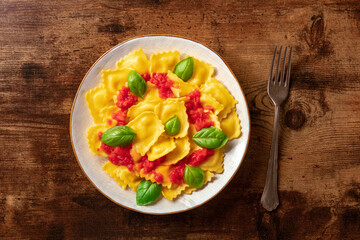 Ravioli with tomato sauce and fresh basil on a plate, shot from the top on a rustic wooden background. Simple healthy Italian dish