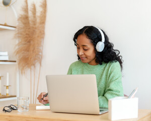 African-american female taking notes while listening to audio podcast in headphones. Online course